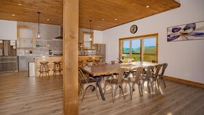 A modern kitchen with wooden ceiling beams, a dining area with a large table and metal chairs, and a view of the outdoors through a window. - A Piece Of Perfect: Pool, Mtn Views, Home Theater, Game Room, Hot Tub, Wifi (Sevierville)