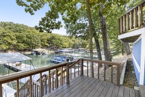 Une terrasse en bois offrant une vue sur un lac, des bateaux et une colline boisée.