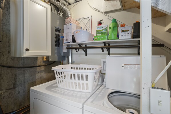 Un espace dédié à la lessive, comprenant un lave-linge, un étendoir et une étagère avec des produits de nettoyage.