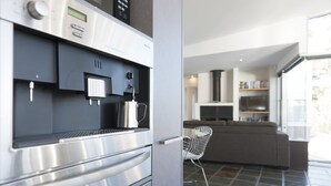 A modern kitchen with a built-in coffee machine, a stainless steel oven, and a grey tiled floor.