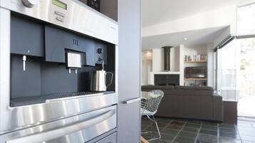 A modern kitchen with a built-in coffee machine, a stainless steel oven, and a grey tiled floor.