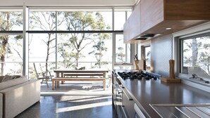 A modern kitchen with large windows, a dining area with a bench, and a view of trees.