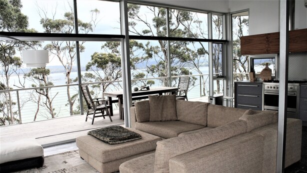 A modern living room with a large window overlooking a scenic view, a cozy sofa, and a dining area with a table and chairs.