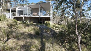 A modern two-story house with a balcony, surrounded by natural bushland and trees.