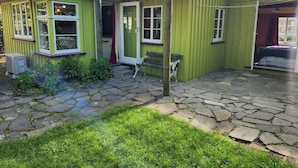 Un edificio verde con un patio de piedra y una zona cubierta.