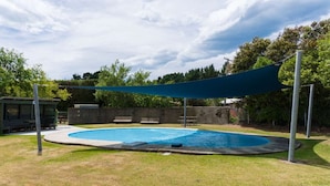 Una piscina con zona sombreada, rodeada por un césped y árboles.