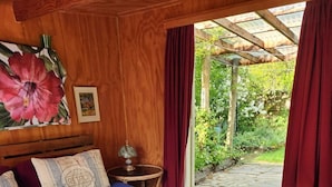 Un dormitorio con cama, mesita de noche, lámpara y vista a un jardín por una puerta de vidrio.