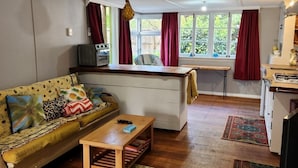 Una sala de estar acogedora con un sofá, una mesa de centro y una alfombra estampada. Se observa, al fondo, una zona de cocina con una mesa de comedor y sillas.