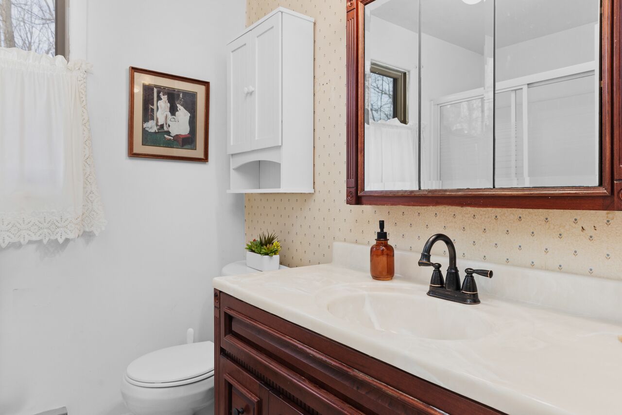 A bathroom with a white toilet, a white vanity with a mirror, a sink with a black faucet, and a framed picture on the wall.