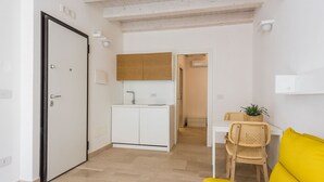 Ein modernes, kompaktes Wohnzimmer mit Küchenzeile, einem Essbereich mit gelbem Sofa und einem separaten Badezimmer.