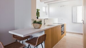 A modern kitchen with a white countertop, wooden cabinets, and a built-in oven. There are two wicker chairs and a potted plant on the counter. - Giudecca's Studio with Terrace by Wonderful Italy (Siracusa)