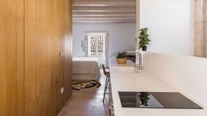 A modern, compact room with a wooden wardrobe, a bed, a small table with a plant, and a black induction cooktop. - Giudecca's Studio with Terrace by Wonderful Italy (Siracusa)