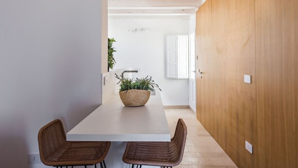 A modern kitchen with a white countertop, two wicker chairs, and a woven basket with a plant. - Giudecca's Studio with Terrace by Wonderful Italy (Siracusa)