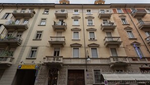 Un edificio a più piani con balconi, un ingresso a livello strada e un segnale che indica un'area di parcheggio.