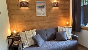 Een gezellige kamer met een grijze bank, twee wandlampen en een poster van Courchevel.