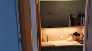 Een kleine keuken met donkere kastjes, een houten aanrechtblad en basis keukenbenodigdheden.