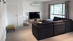 Uma sala de estar moderna com um sofá seccional, uma TV de tela plana e uma grande janela com cortinas.