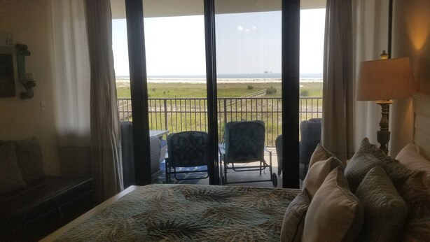 Een hotelkamer met een bed, een stoel, een tafel en uitzicht op het strand.