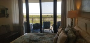 A hotel room with a bed, a chair, a table, and a view of the beach.