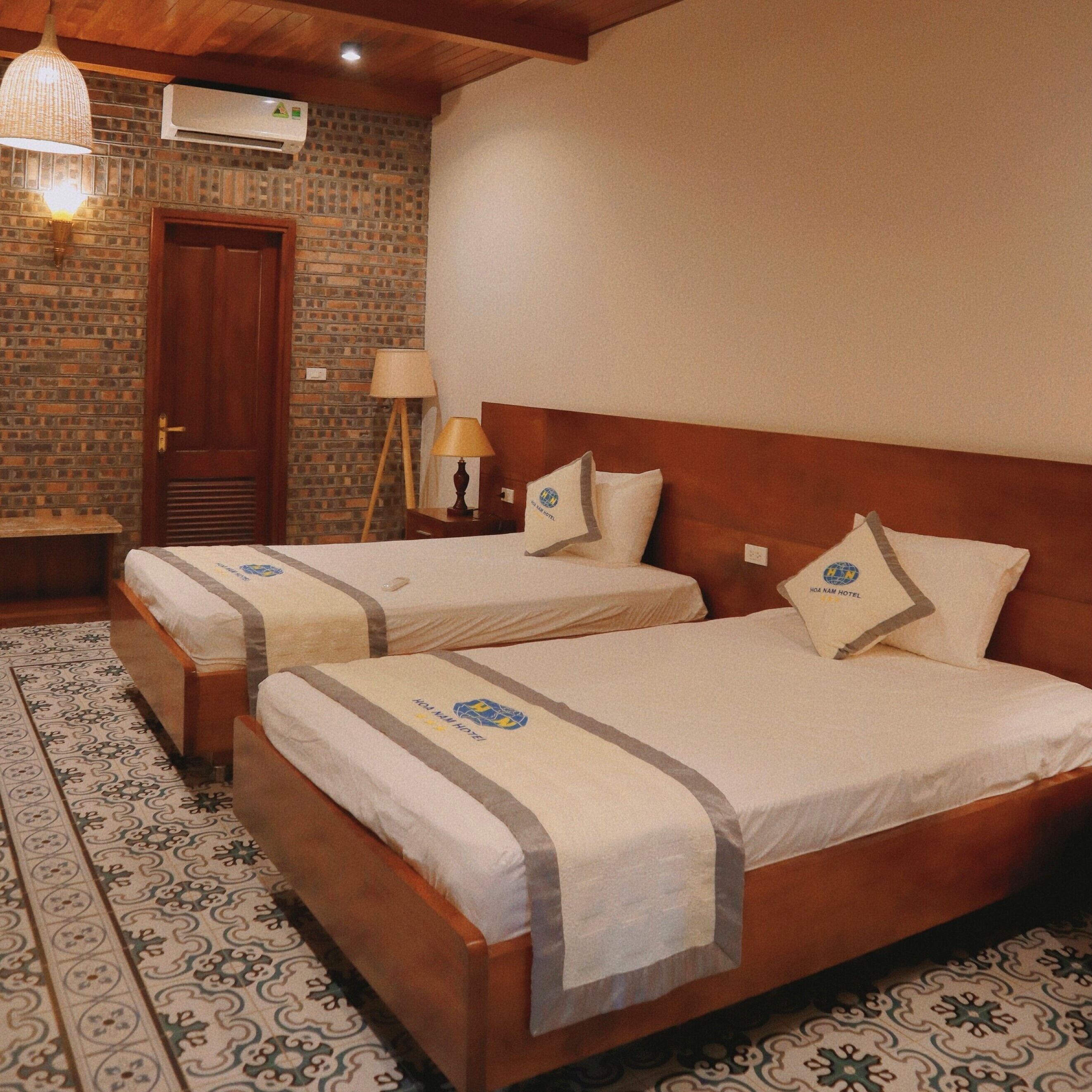 A hotel room with two wooden beds, a brick wall, an air conditioning unit, and patterned floor tiles.
