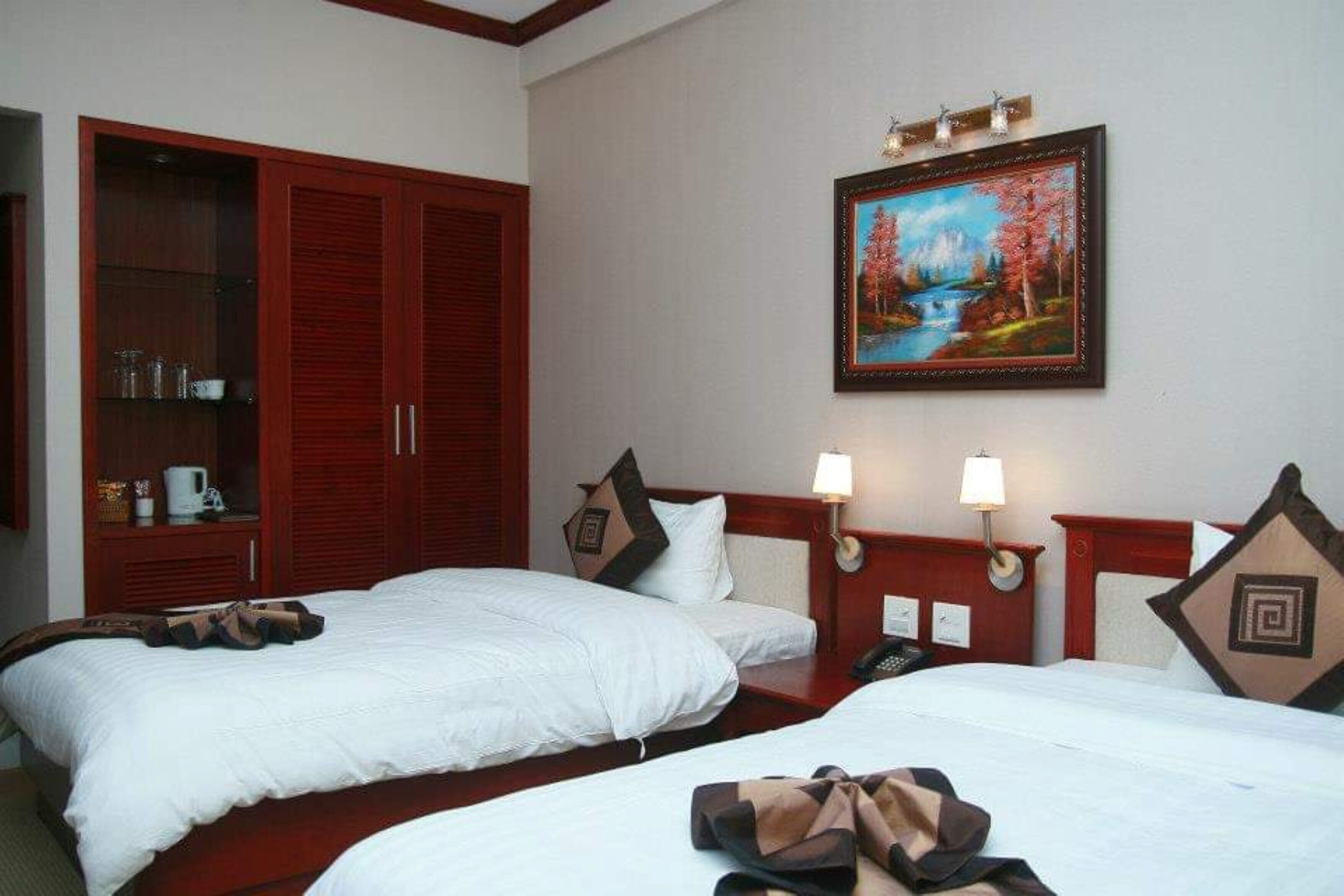 A hotel room with two beds, a wardrobe, a painting, bedside lamps, and a telephone.