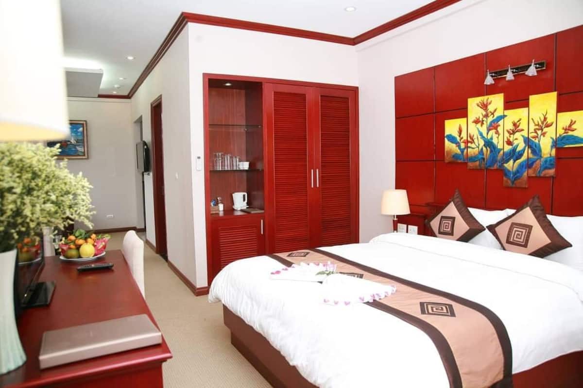 A hotel room with a large bed, a wardrobe, a desk with a lamp, and a painting on the wall.