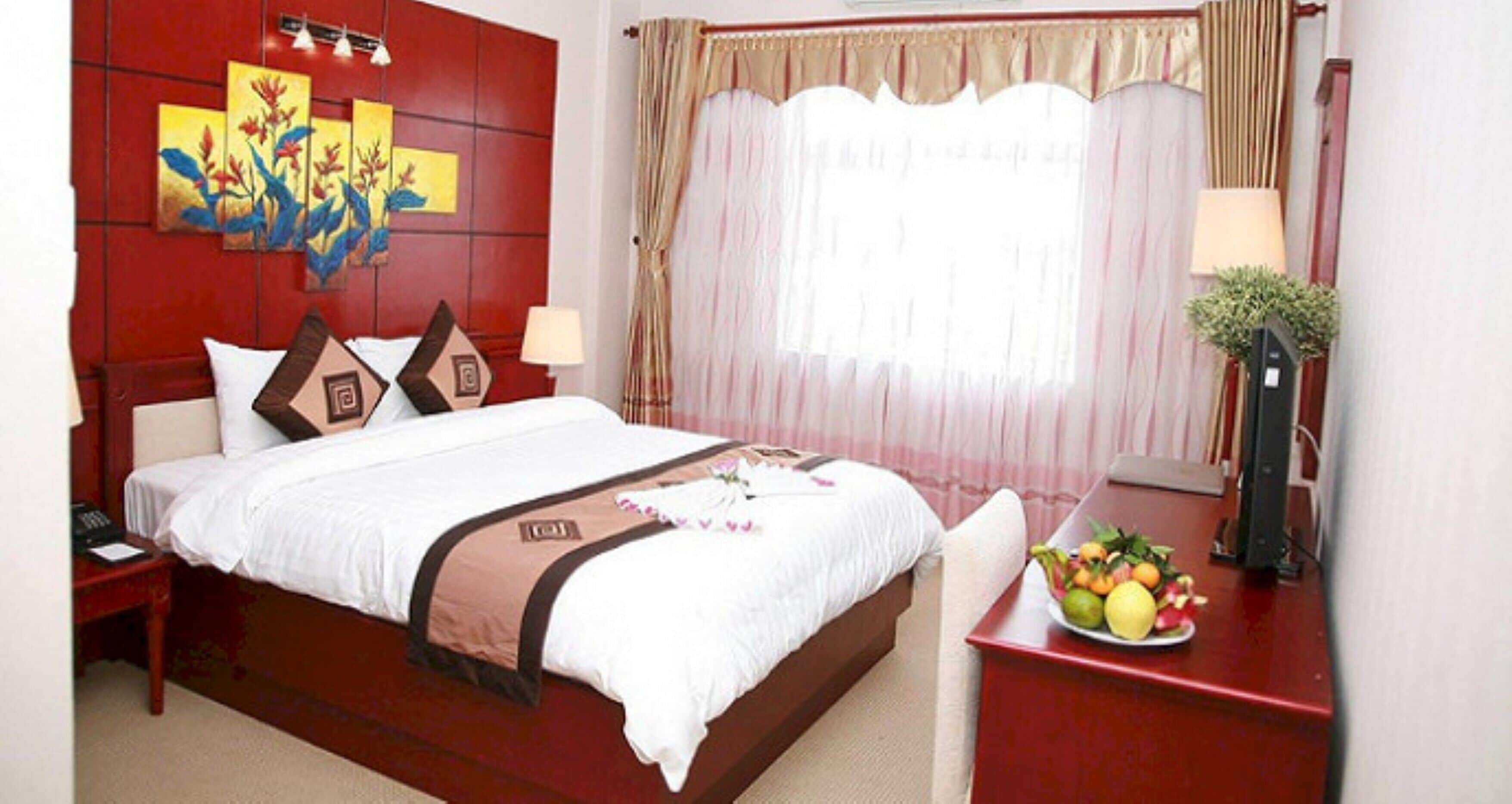 A hotel room with a large bed, a bedside table with a lamp, a fruit bowl, and a painting on the wall.