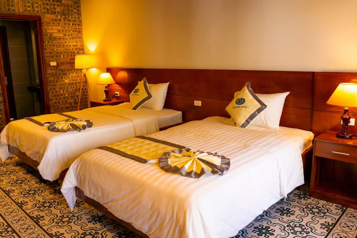 A hotel room with two beds, a brick wall, and patterned floor tiles.