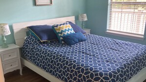 A bedroom with a bed, two bedside tables, a window with blinds, and a wall-mounted picture. - “Truly Beautiful”.    Golf Course & Lake View Getaway – Minutes from the Beach! (Pawleys Island)