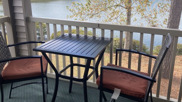 A covered outdoor area with a table and two chairs, overlooking a lake and trees. - “Truly Beautiful”.    Golf Course & Lake View Getaway – Minutes from the Beach! (Pawleys Island)