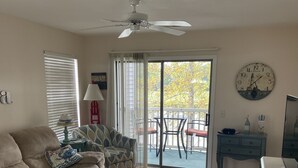A living room with a beige sofa, patterned armchair, and a large beach-themed rug. A ceiling fan, a clock, and a small table with decorative items are also visible. - “Truly Beautiful”.    Golf Course & Lake View Getaway – Minutes from the Beach! (Pawleys Island)
