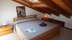 A bedroom with a wooden bed, a nightstand, a bedside lamp, a mirror, and a skylight. - Beautiful Attic Apartment Near the Centre of Lignano Sabbiadoro (Lignano Sabbiadoro)