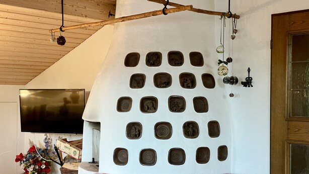 Une pièce dotée d’un décor mural original, avec de nombreuses découpes carrées, un plafond en bois, un téléviseur à écran plat, une table en bois agrémentée de coussins décoratifs et une porte avec des panneaux de verre.