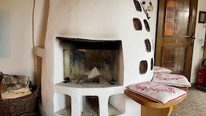 Une cheminée avec un manteau en pierre, un banc en bois avec des coussins et une porte dotée d’un panneau de verre.