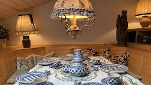 Un coin repas avec une table dressée pour le thé, agrémenté de vaisselle bleue et blanche à motifs et d’une nappe décorative.