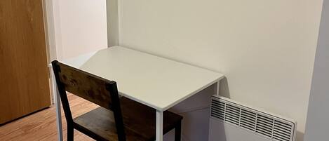 Uma pequena mesa branca com uma cadeira de madeira num quarto com soalho de madeira e parede branca.