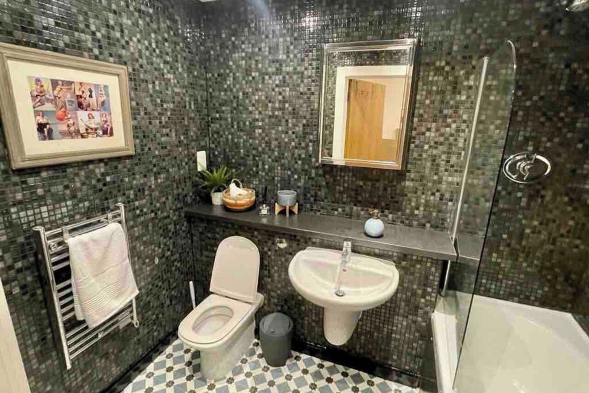 A bathroom with a mosaic tile wall, a toilet, a sink, and a shower.