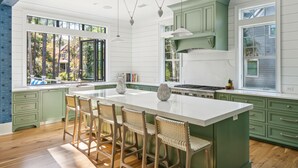A spacious kitchen with a large island, green cabinets, and a view of the outdoors. - Stunning Coastal Gem in Vanderhorst with private pool (Kiawah Island)