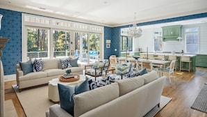 A spacious living room with a large window, a dining area, and a kitchen with green cabinets. - Stunning Coastal Gem in Vanderhorst with private pool (Kiawah Island)
