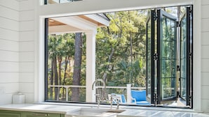 A modern kitchen with green cabinets, a white countertop, and a large window offering a view of the outdoors. - Stunning Coastal Gem in Vanderhorst with private pool (Kiawah Island)
