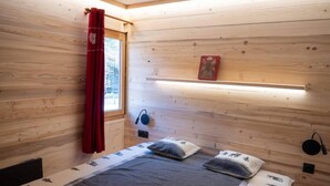 Una accogliente camera da letto in legno con un letto, una finestra con tende rosse, uno scaffale con un oggetto decorativo e una lampada fissata al muro.