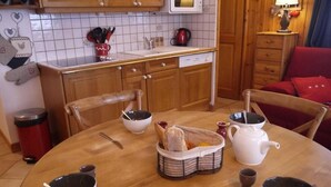 Una cucina accogliente con mobili in legno, zoccolo paraschizzi in piastrelle e un tavolo da pranzo apparecchiato con ciotole, un teiera e un cesto di pane.