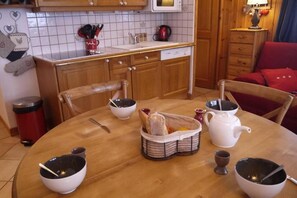 A cozy kitchen with wooden cabinets, a tiled backsplash, and a dining table set with bowls, a teapot, and a basket of bread. - 150m from shops, 1st floor, balcony, tv, 40m², Méribel-Mottaret (Méribel - Les Allues)