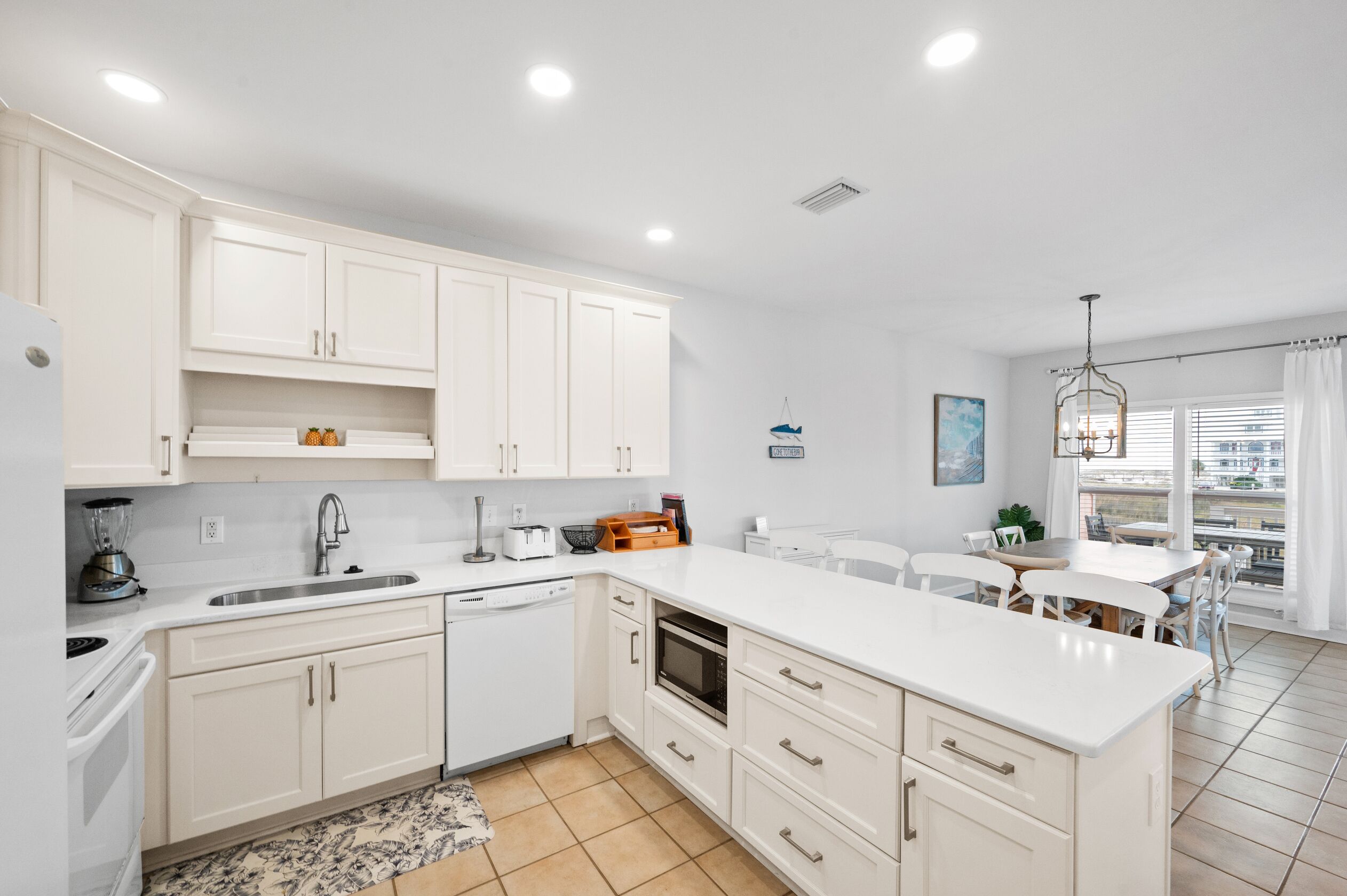 A modern kitchen with white cabinets, a central island, and a dining area with a view.