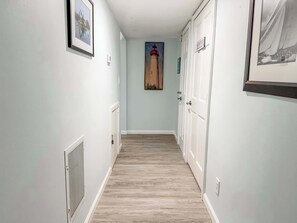 Un pasillo con paredes azul claro, piso de madera y puertas blancas. Hay cuadros en las paredes y un cuadro de un faro al fondo.