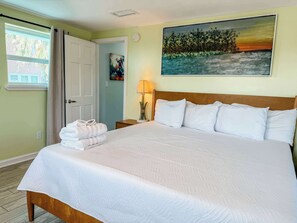 A neatly made bed with white linens, a wooden headboard, and a painting of a landscape on the wall.