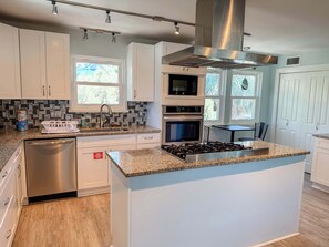 A modern kitchen with white cabinets, a granite countertop, stainless steel appliances, and a central island. - St.George Island Bayfront Paradise with Pool,Dock Golf Cart Included (St. Geroge Island)