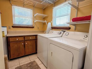 A laundry area with a washing machine, dryer, wooden cabinets, and two windows with blinds. - St.George Island Bayfront Paradise with Pool,Dock Golf Cart Included (St. Geroge Island)
