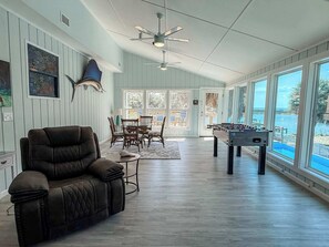 A spacious room with a leather sofa, a foosball table, and a dining area with chairs and a table. - St.George Island Bayfront Paradise with Pool,Dock Golf Cart Included (St. Geroge Island)
