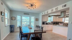 A spacious kitchen with white cabinets, a dining table with chairs, and a large window with blinds. - St.George Island Bayfront Paradise with Pool,Dock (St. Geroge Island)